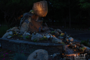 Halogen bulbs illuminate Land of ELITE Landscaping sign.