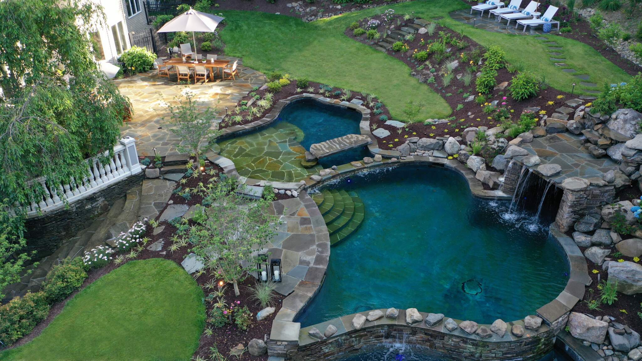 an outdoor living space with a custom pool, waterfall, and patio designed and built by Land of ELITE, the leading outdoor contractor for New York