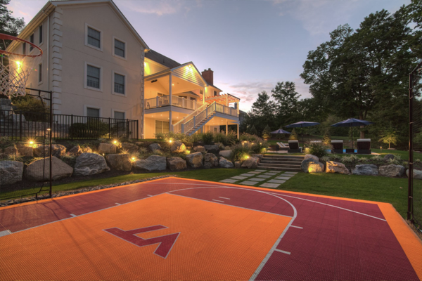 A half-court basketball court illuminated by ample lighting, set amidst a picturesque landscape.