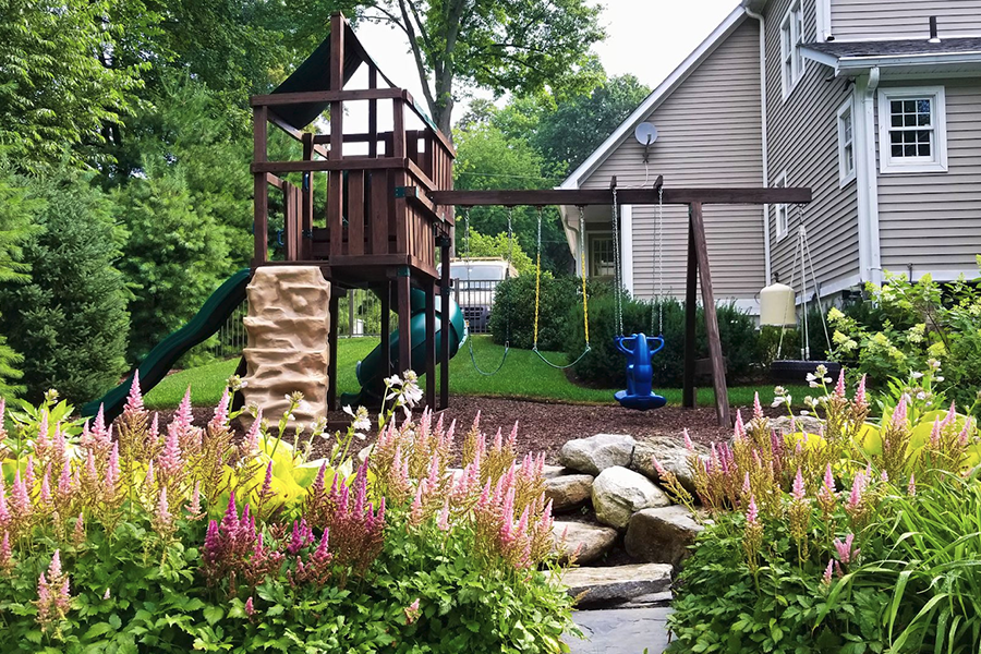 A vibrant backyard playground nestled in a well-maintained lawn, surrounded by a colorful array of flowers concept image for family-friendly landscape