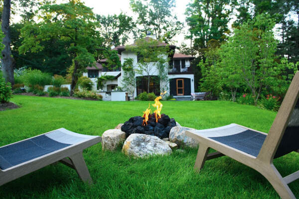 Cozy outdoor firepit area featuring two inviting chairs, embraced by lush greenery and the serenity of nature, perfect for tranquil evenings and warm gatherings.