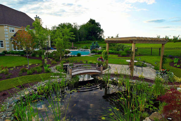 New Rochelle's premier outdoor living contractor creates a scenic oasis with a pool, pond, and charming bridge.