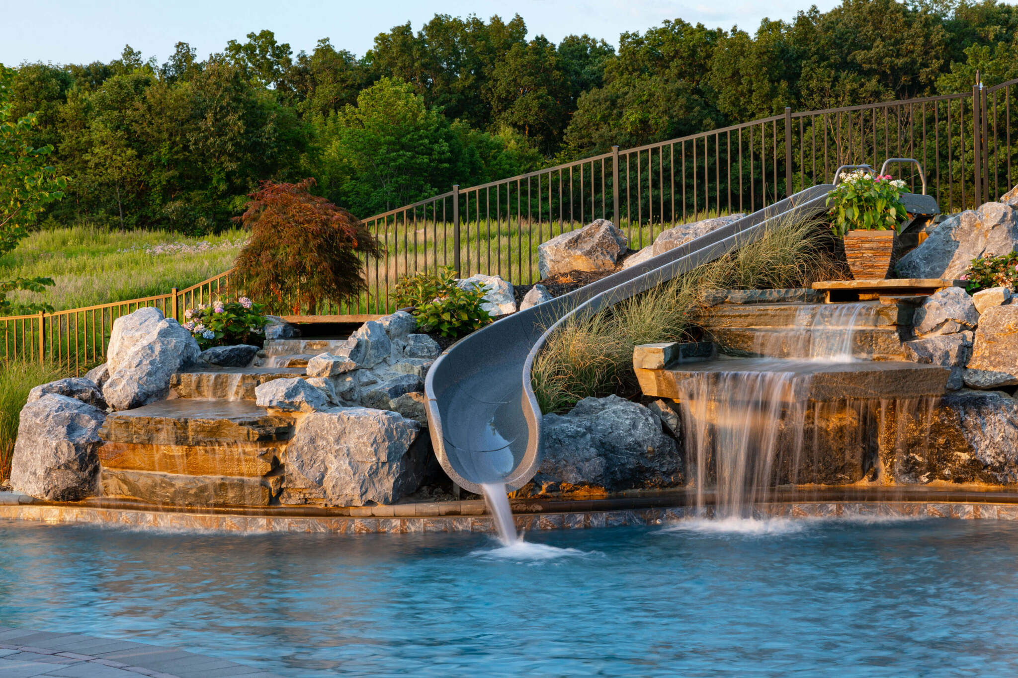 Backyard renovation ideas featuring a pool with a waterslide, cascading waterfall, rocks, and lush greenery for a natural look