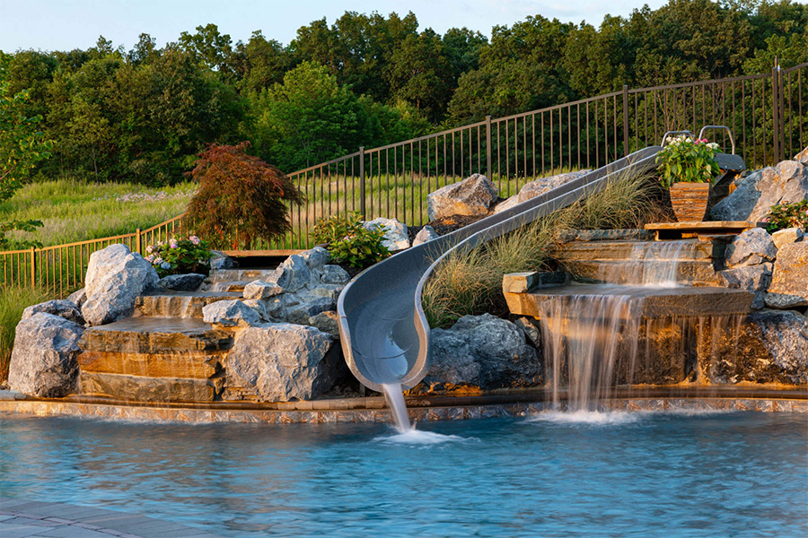 Backyard pool with a waterslide and cascading waterfall, surrounded by lush greenery for a natural, resort-like feel