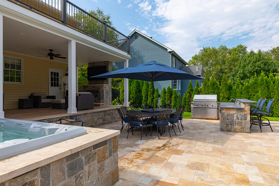 Outdoor patio with dining area, stone hardscaping, built-in grill, and hot tub in a hardscaping luxury landscape setting