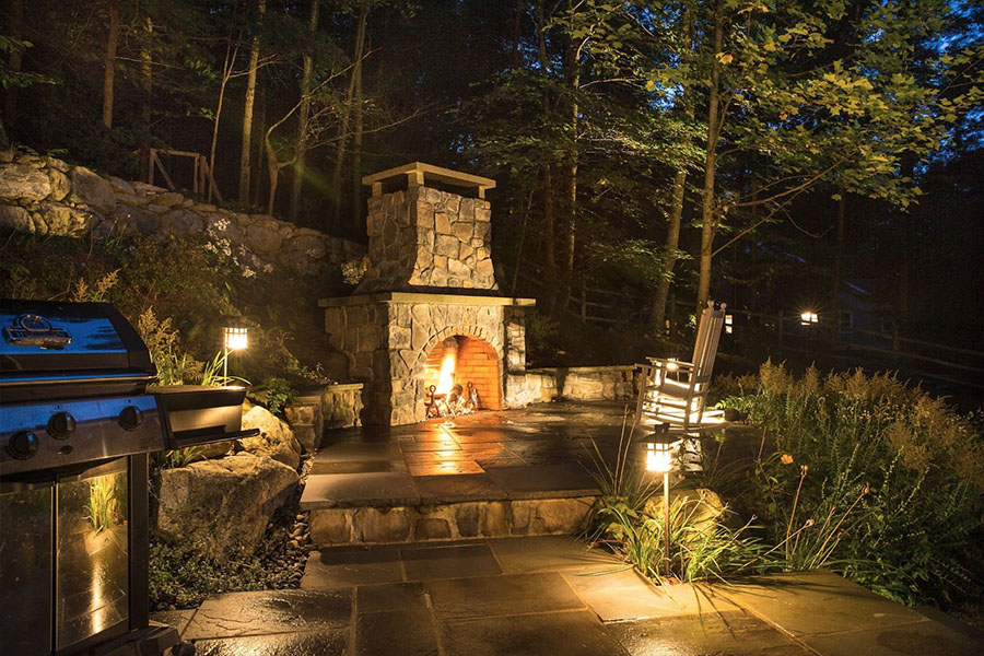 Patio with a stone fireplace, illuminated for nighttime enjoyment, emphasizing premium outdoor living features