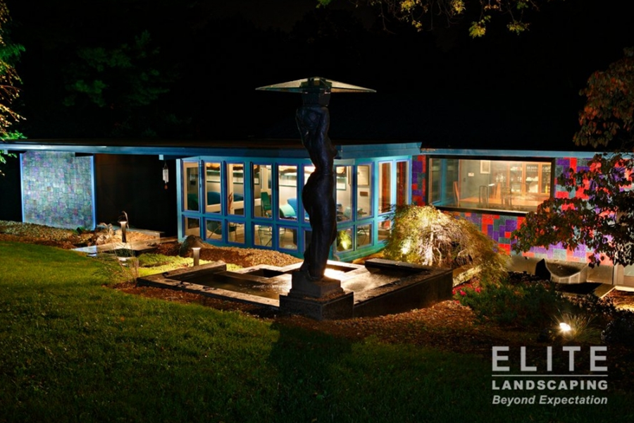 Nighttime view of outdoor winter living space with lighting, a sculpture, and an enclosed patio, offering warmth and style